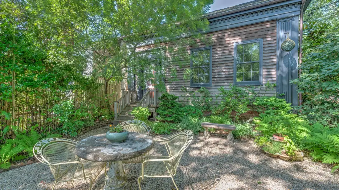 A shaded outdoor patio with a round table and seating beside a house.