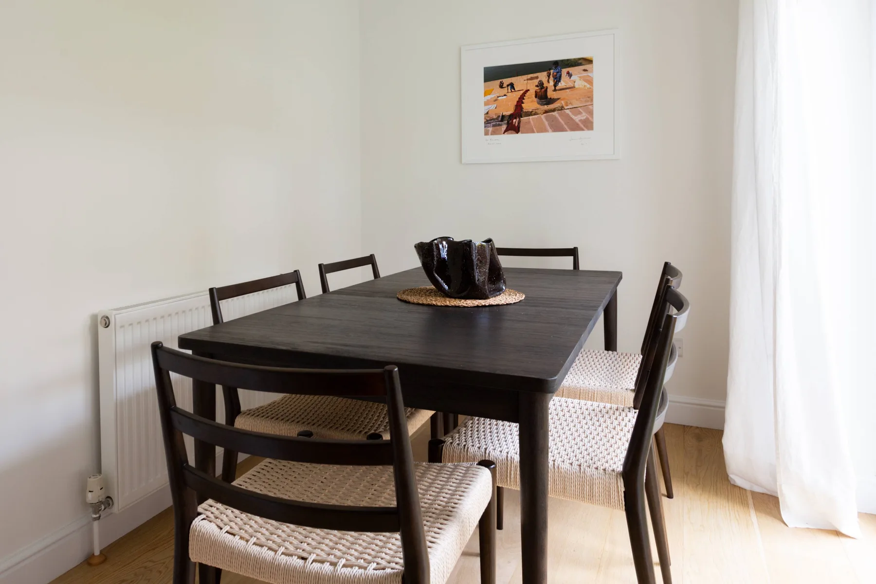 Una mesa de comedor con asientos tejidos está junto a una ventana luminosa.