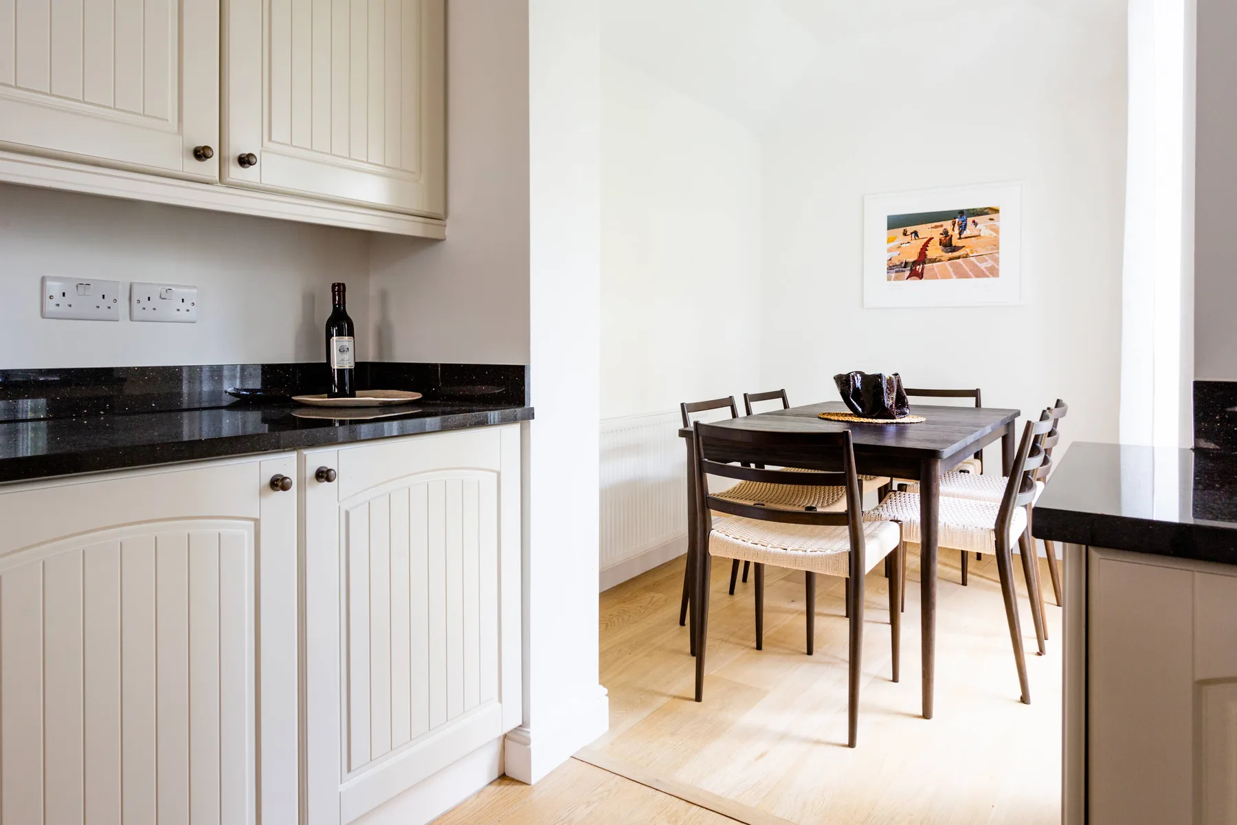 Un comedor con una mesa de madera y sillas junto a armarios blancos de cocina.