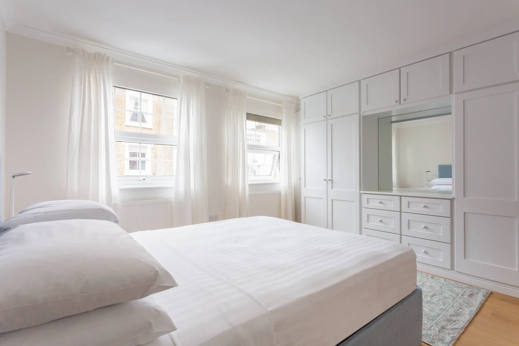 Un dormitorio luminoso con una cama tendida y armarios empotrados.