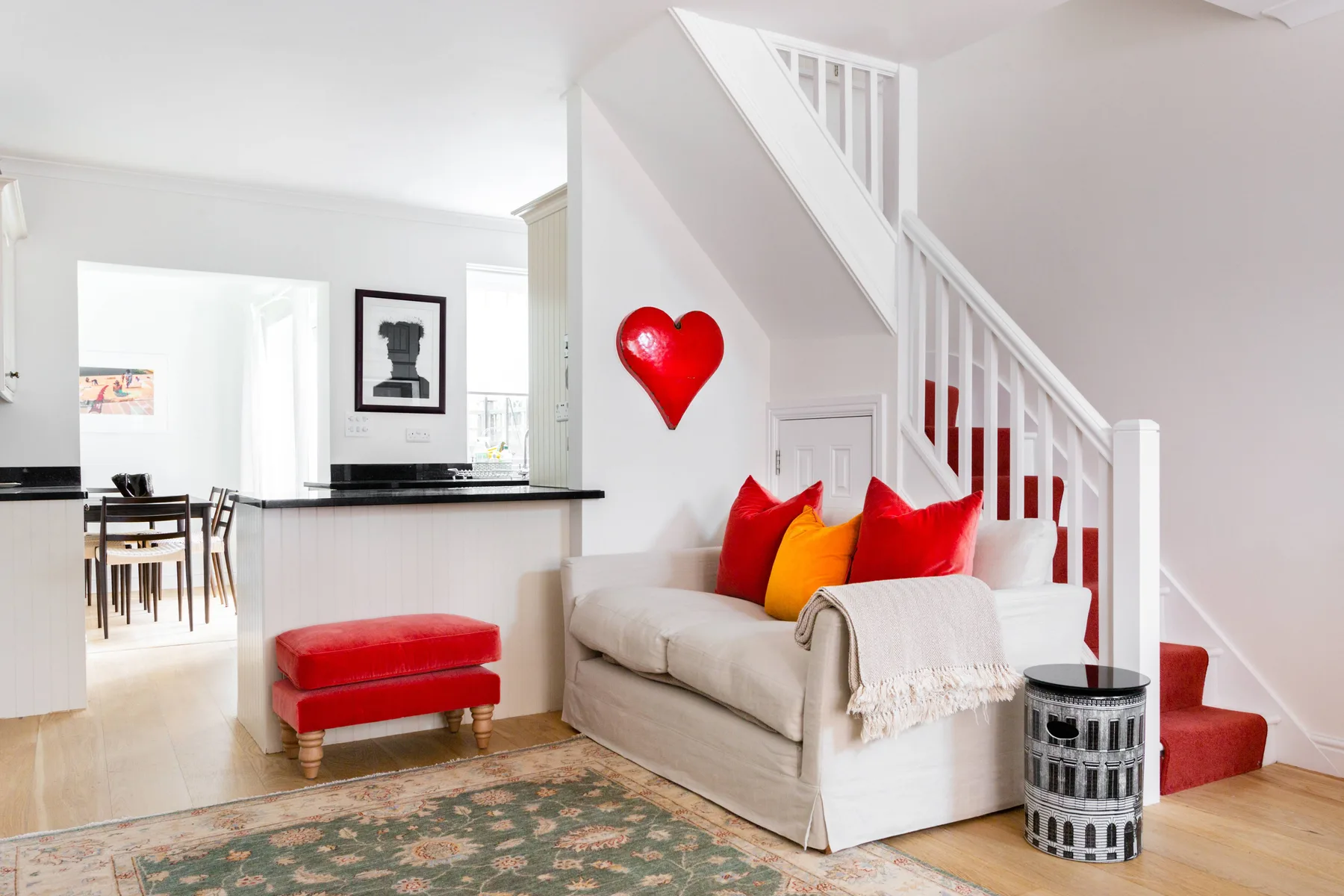 Una sala luminosa con un sofá color crema bajo una escalera.