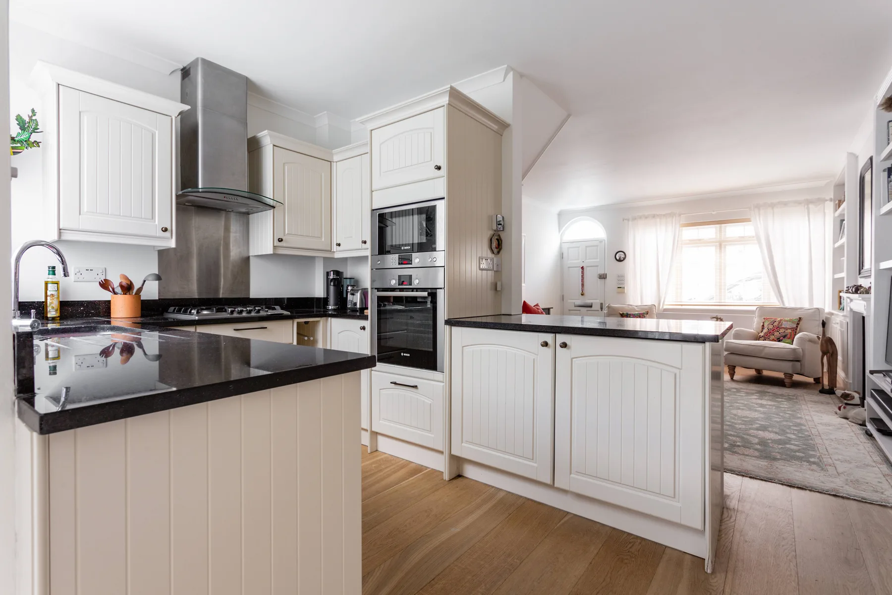 Una cocina luminosa con gabinetes blancos y una encimera negra se abre a una sala de estar.