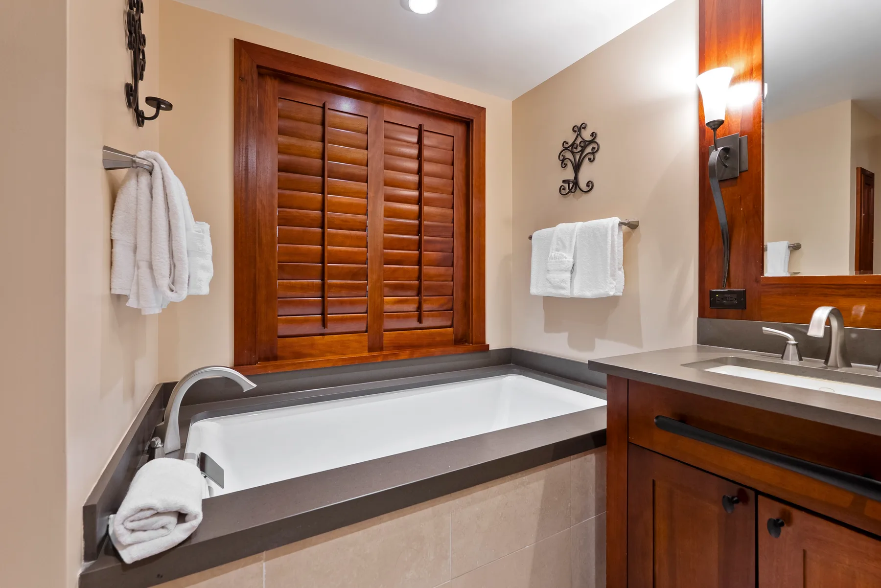 Un baño con bañera empotrada, persianas de madera y lavabo.