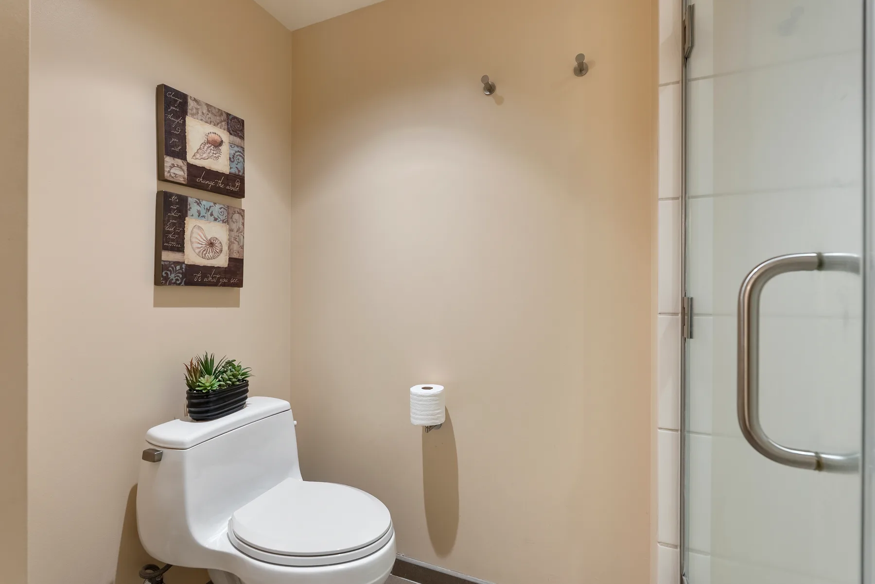 Un baño con un inodoro, arte en la pared y una ducha con panel de vidrio.