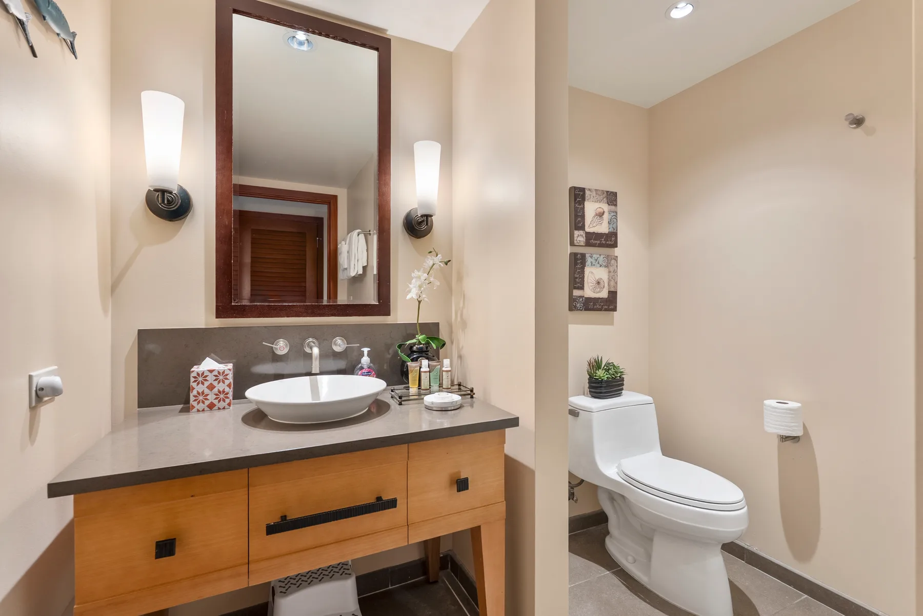 Un tocador de baño con lavabo y espejo junto a un inodoro.