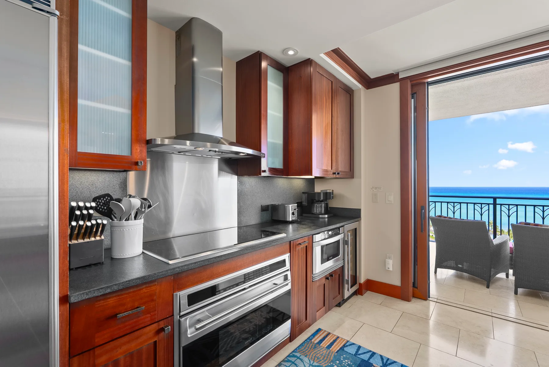 Una cocina moderna con gabinetes de madera da a un balcón con vistas al mar.