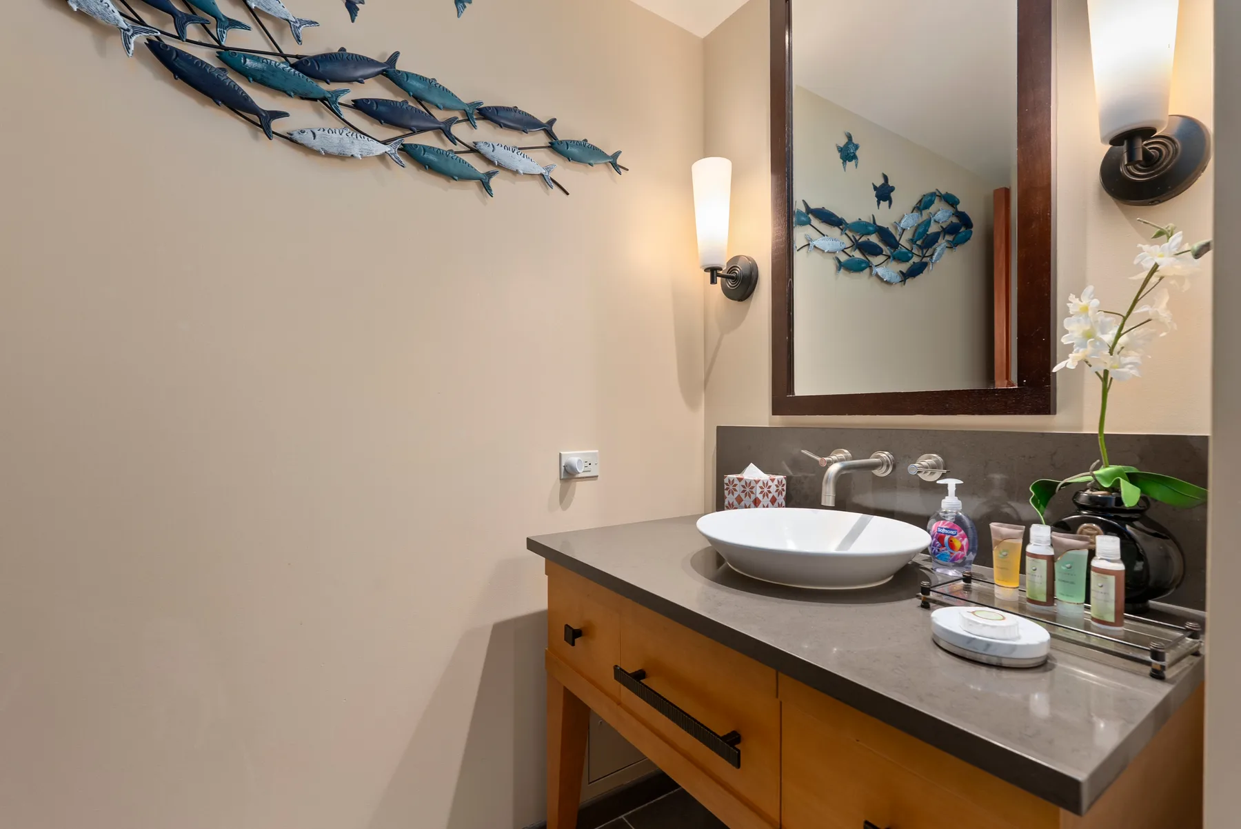 Un tocador de baño con lavabo sobre encimera, espejo y adornos de peces.