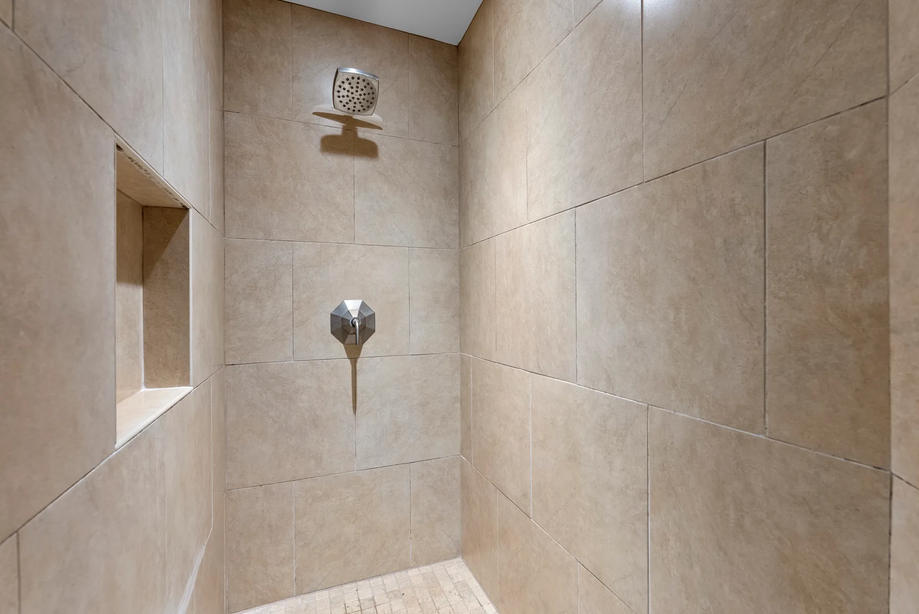 Una ducha con azulejos, rociador y control montados en la pared.