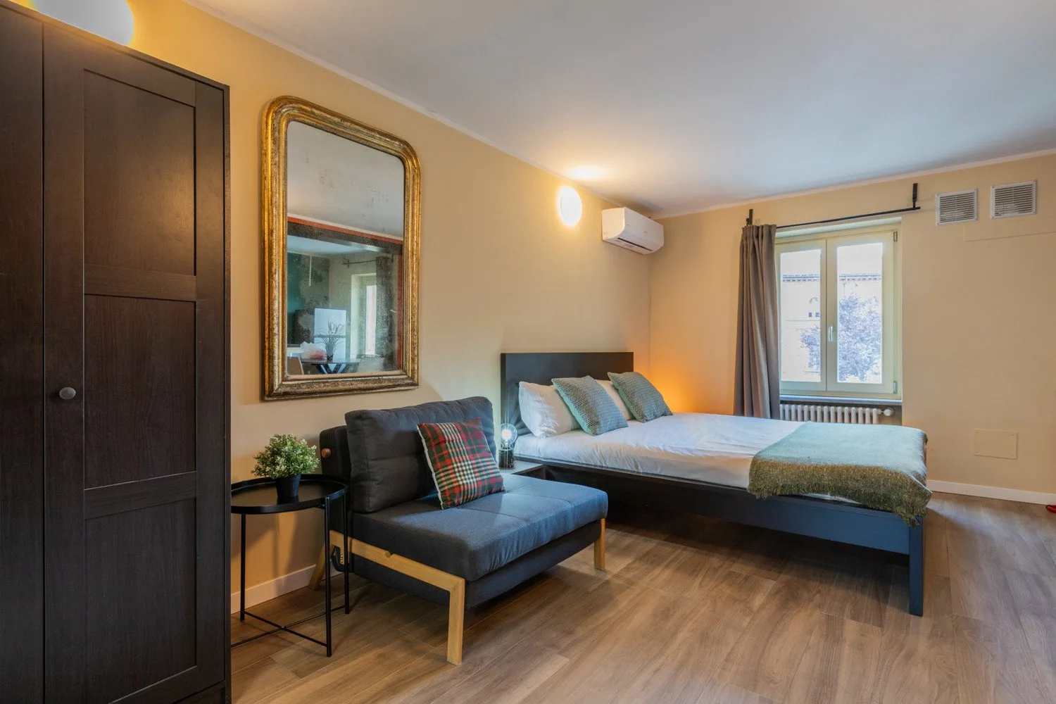 Un dormitorio con una cama, una zona de asientos oscura y una ventana.