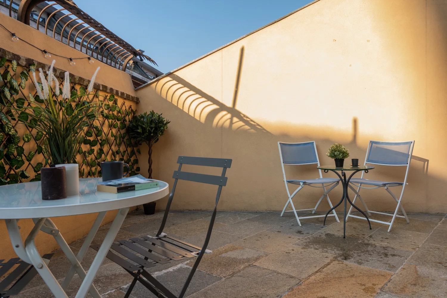 An outdoor patio with tables and chairs beside a sunlit wall.