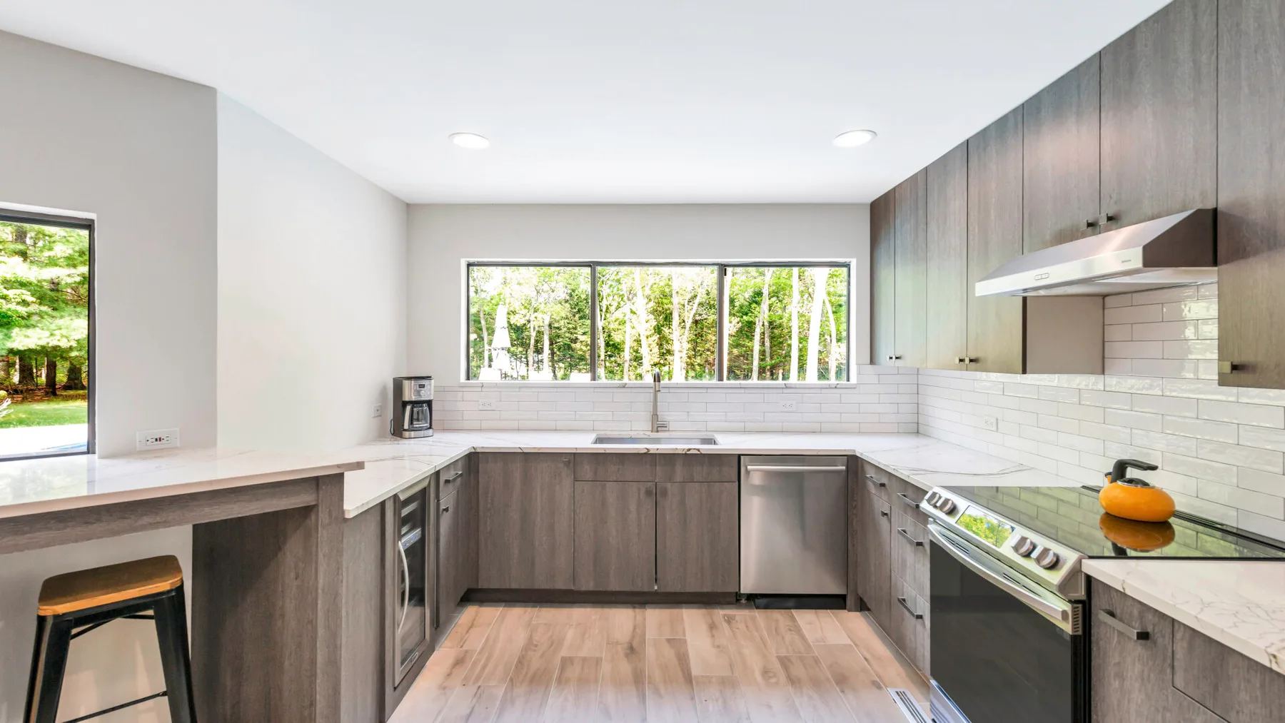 A modern kitchen with dark cabinets, pale countertops, and a wide window.