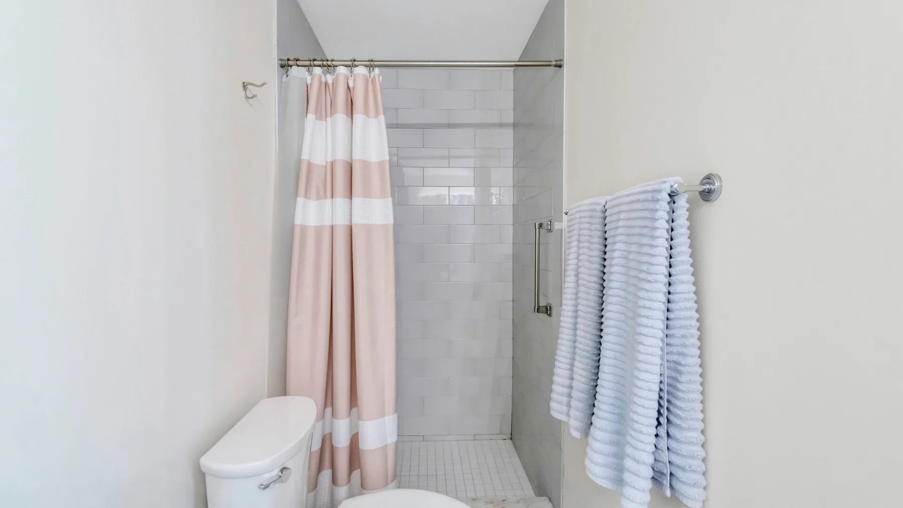 A tiled bathroom shower with a striped curtain and towels hanging nearby.