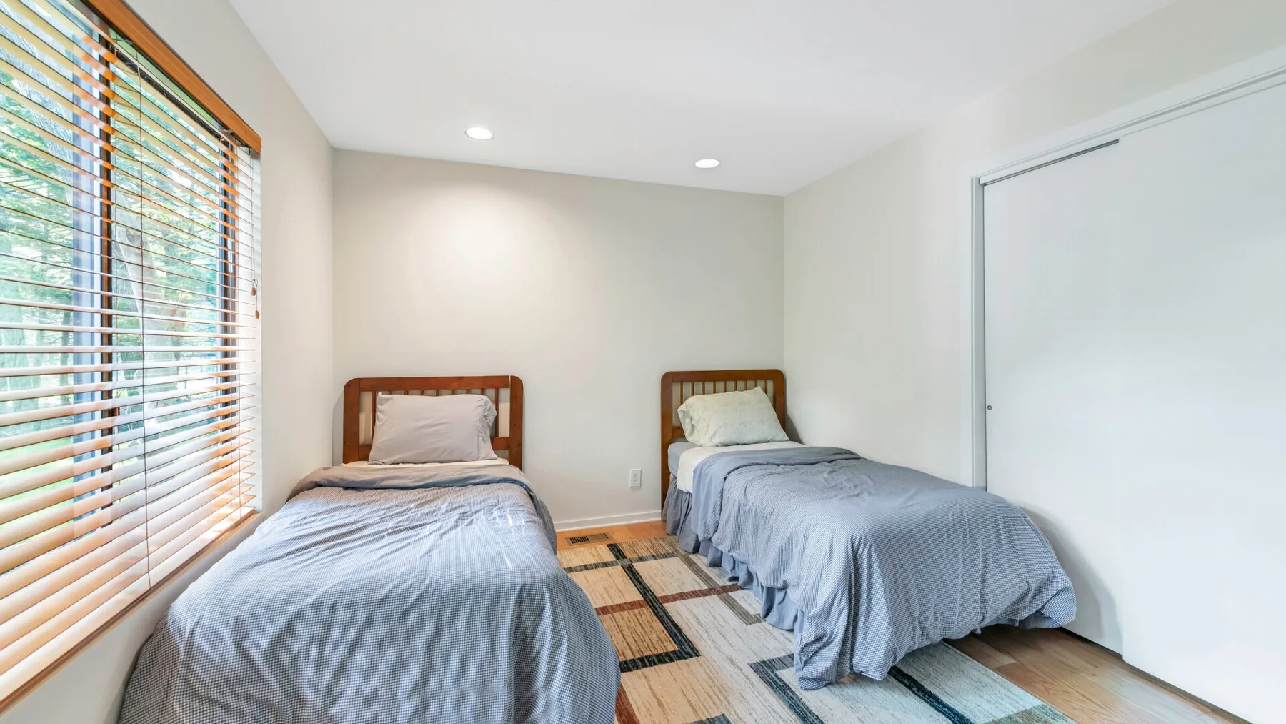 A bedroom with two beds, a window with blinds, and a sliding door.