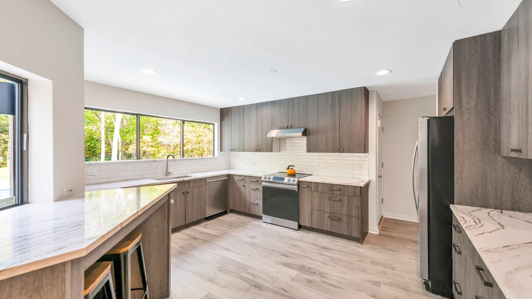 A bright kitchen with wood-toned cabinets, pale countertops, and windows over the sink.