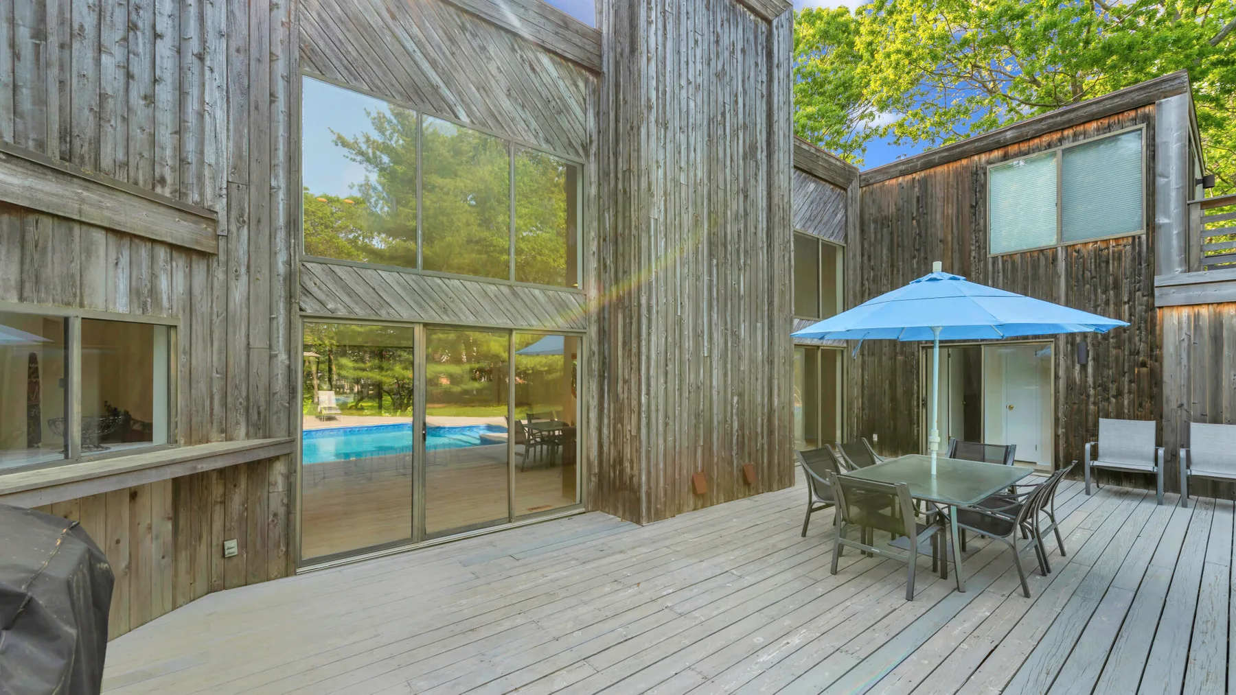 A wooden deck beside a modern home, with outdoor dining furniture and a blue umbrella.