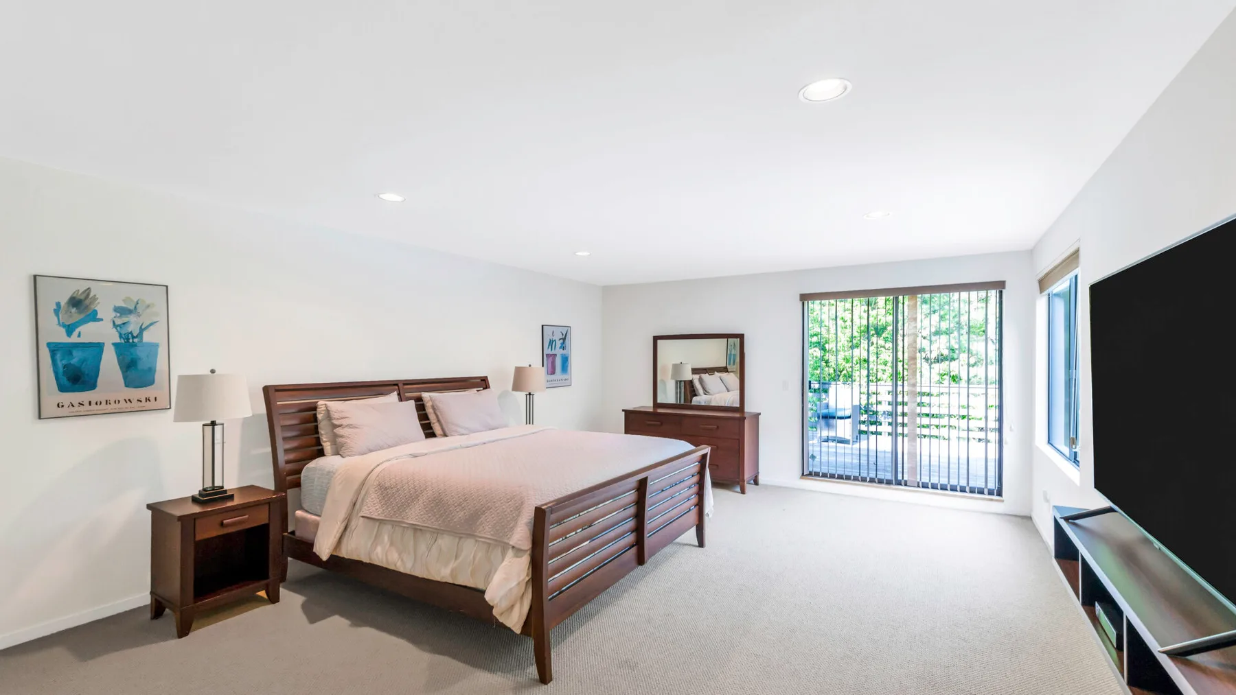 A bright bedroom with a bed, bedside tables, and a large window.
