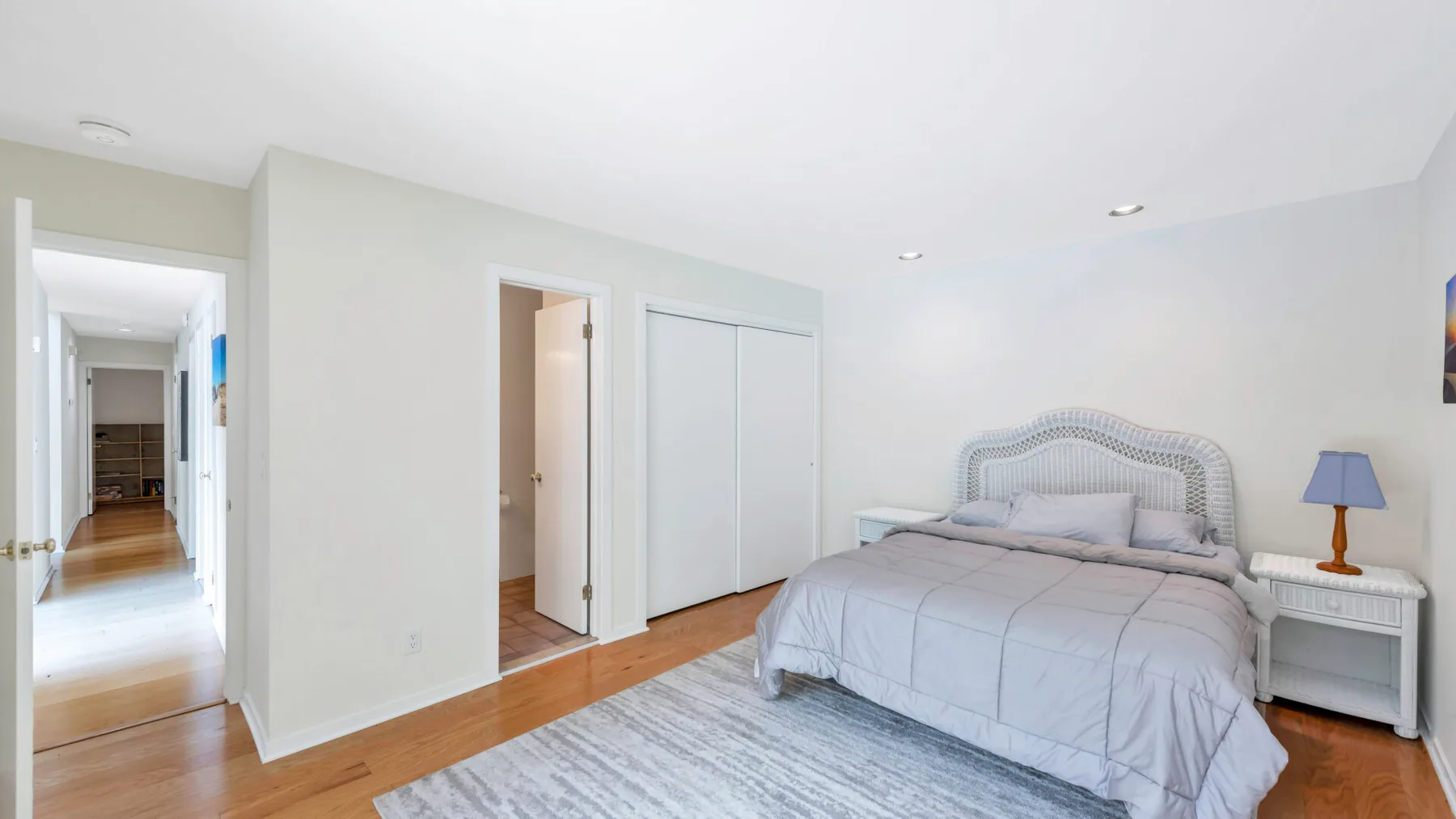 A bright bedroom with a bed, pale bedding, and hardwood flooring.