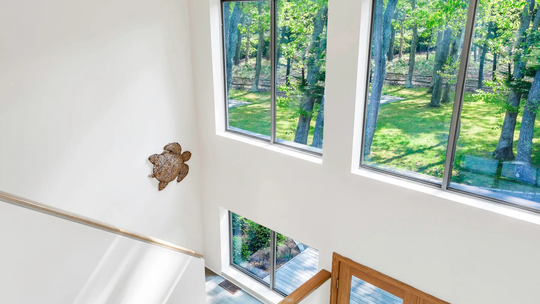 A bright interior stairwell with large windows overlooking a wooded garden.