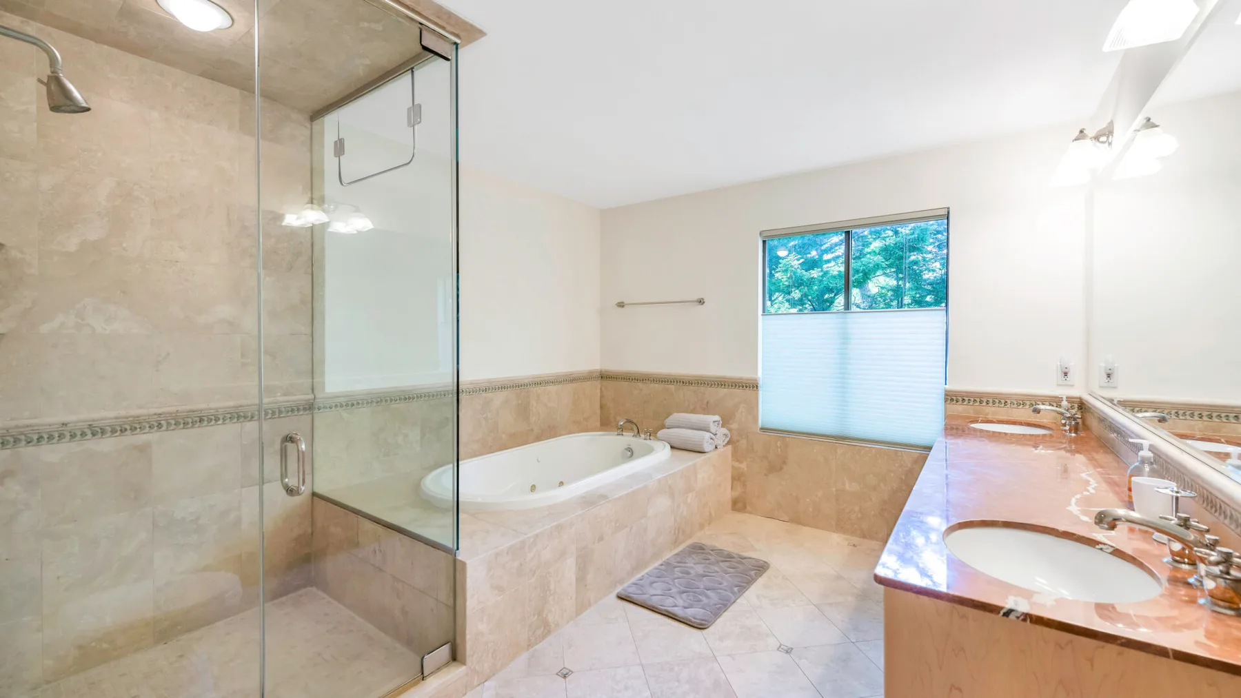 A bright bathroom with a glass shower, bathtub, and double sink.