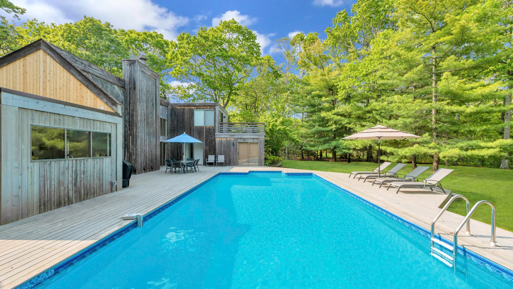 Outdoor swimming pool beside a wooden deck and leafy trees.