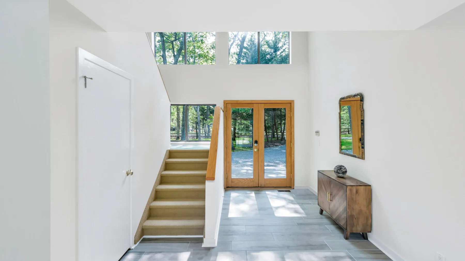 A bright entryway with a staircase, glass doors, and a wooden console.