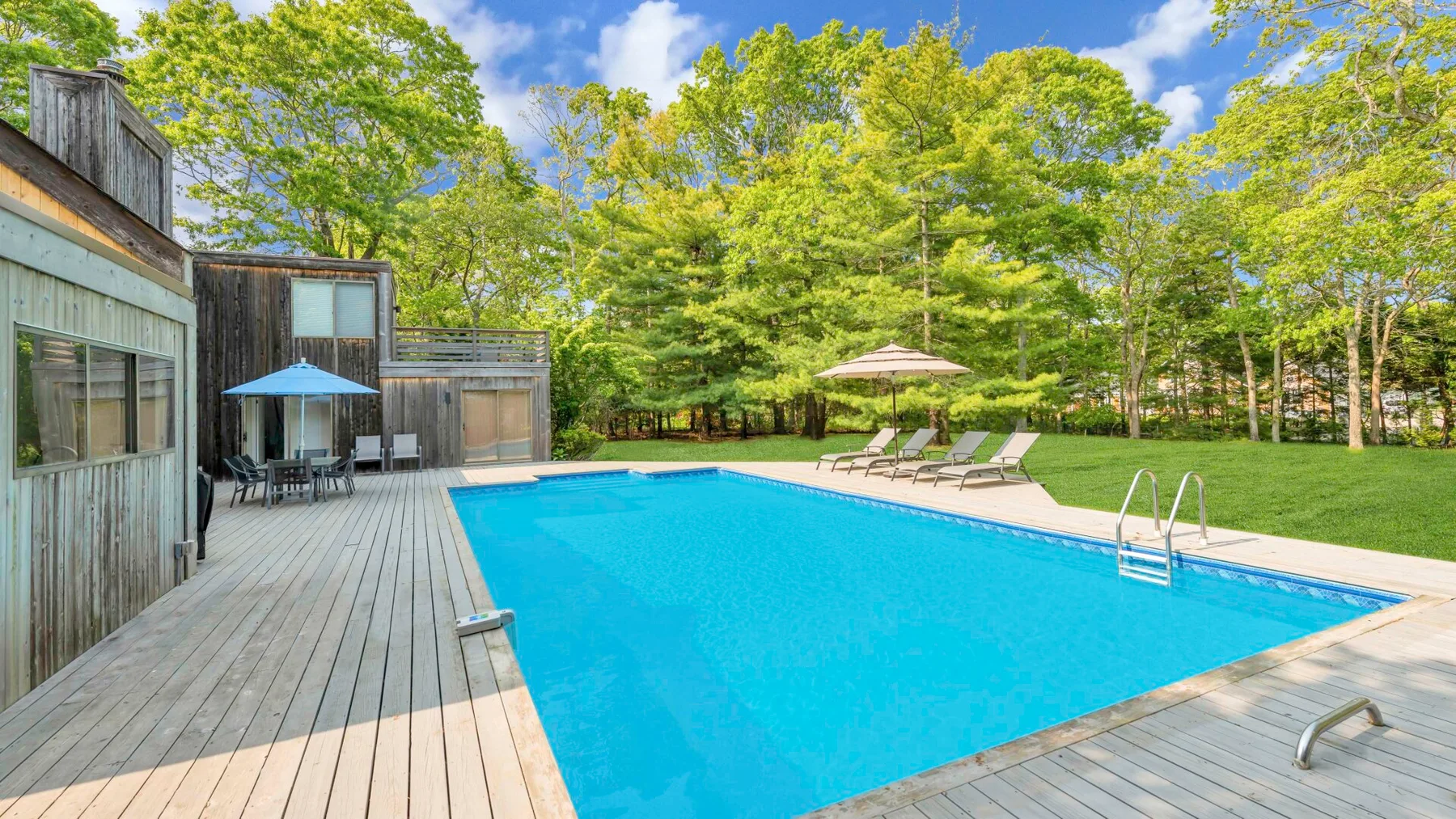 An outdoor swimming pool beside a wooden deck, surrounded by trees.