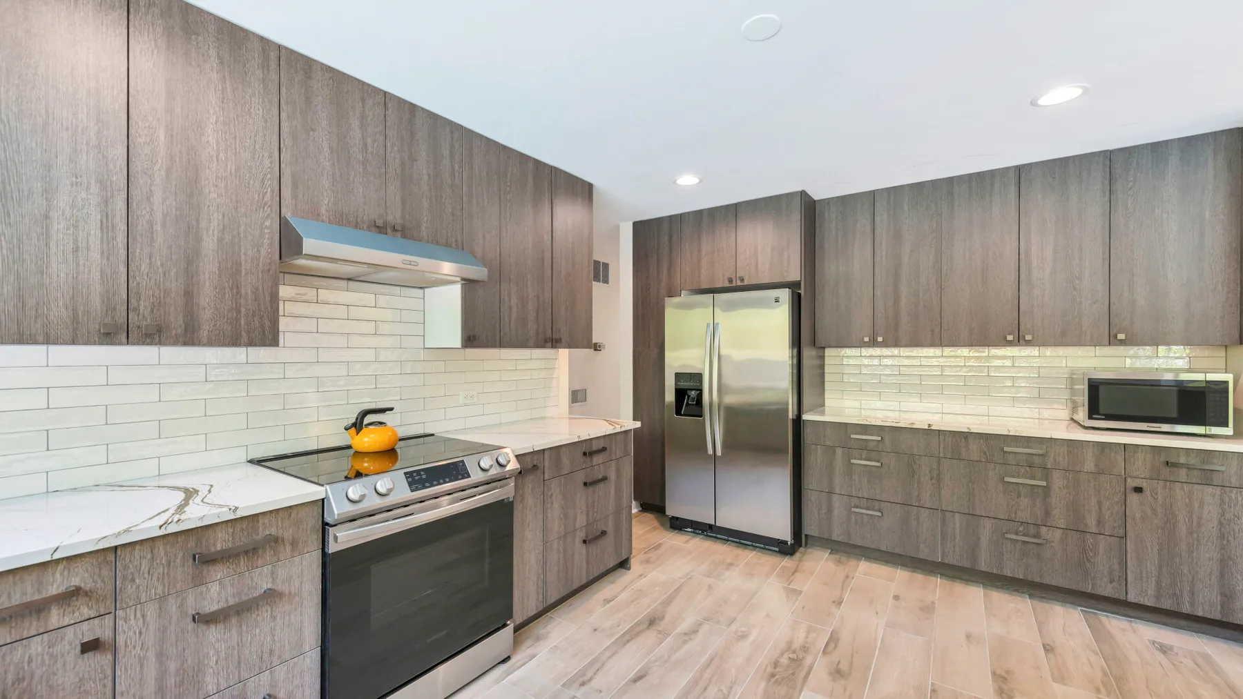 A modern kitchen with wood cabinetry, stainless steel appliances, and light countertops.
