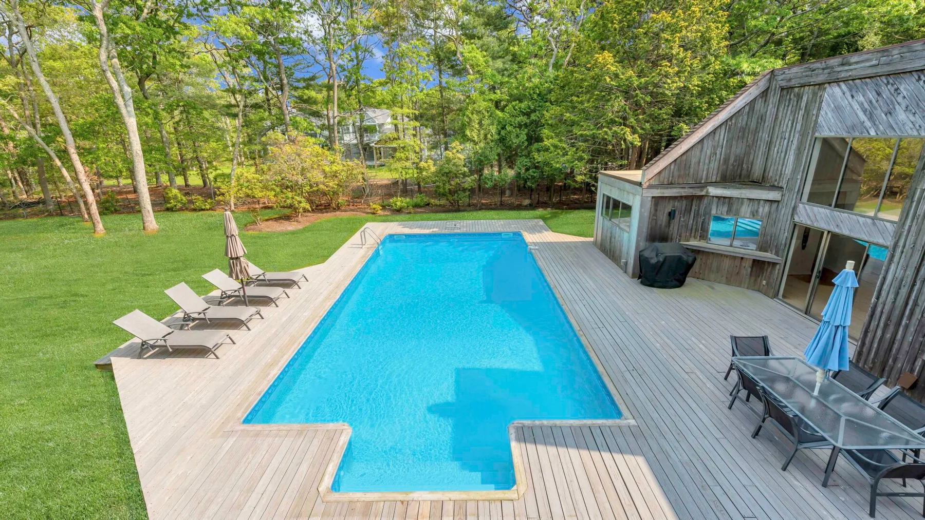 An outdoor swimming pool is surrounded by a wooden deck and green lawn.