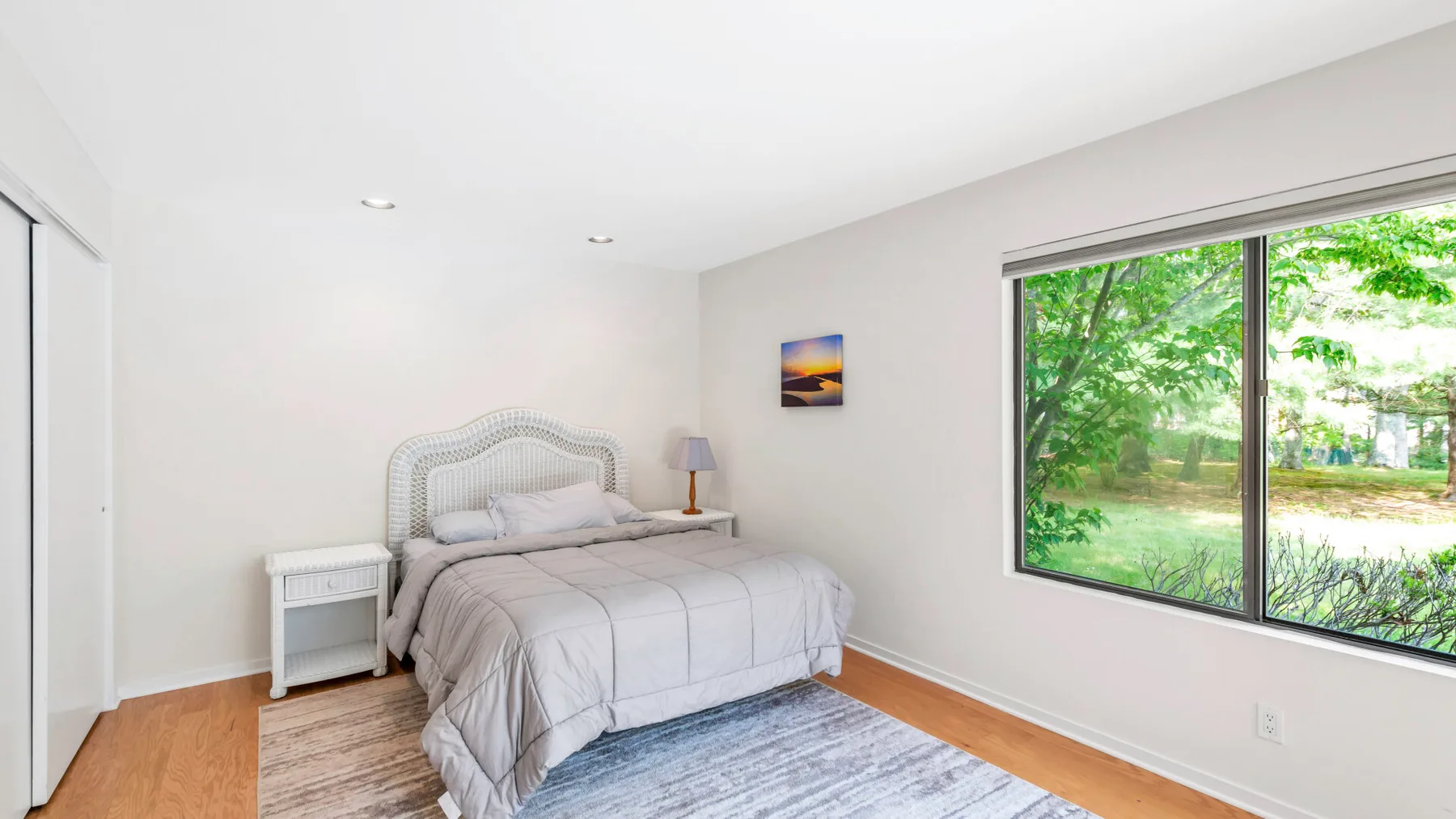 A bright bedroom with a bed beside a large window overlooking greenery.