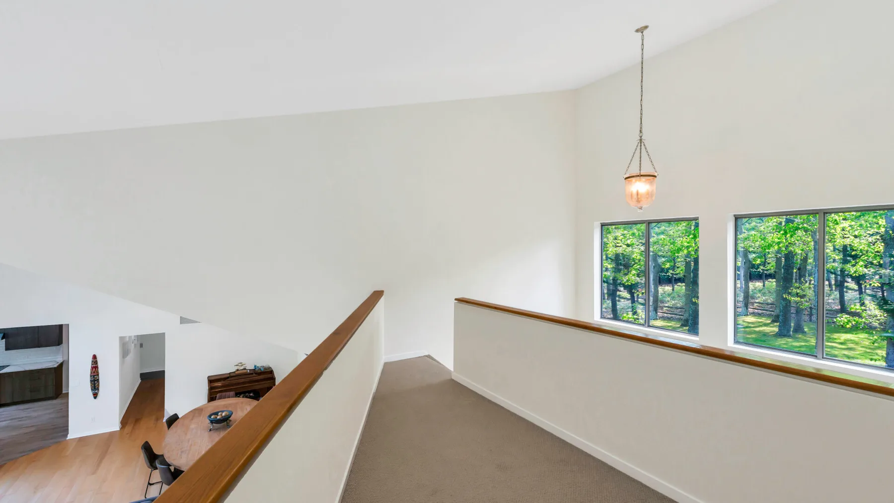 A bright upstairs landing overlooks the living area, with large windows facing leafy trees.