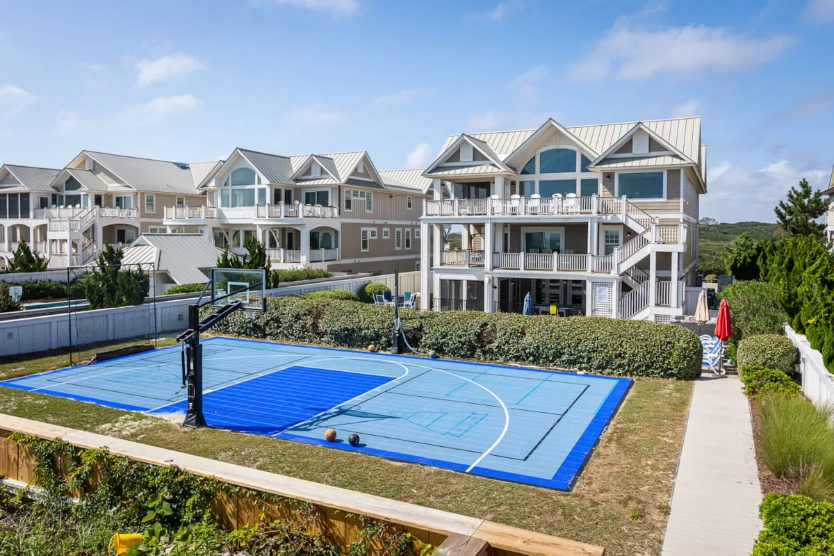 A blue outdoor basketball court sits beside a row of multi-story buildings.