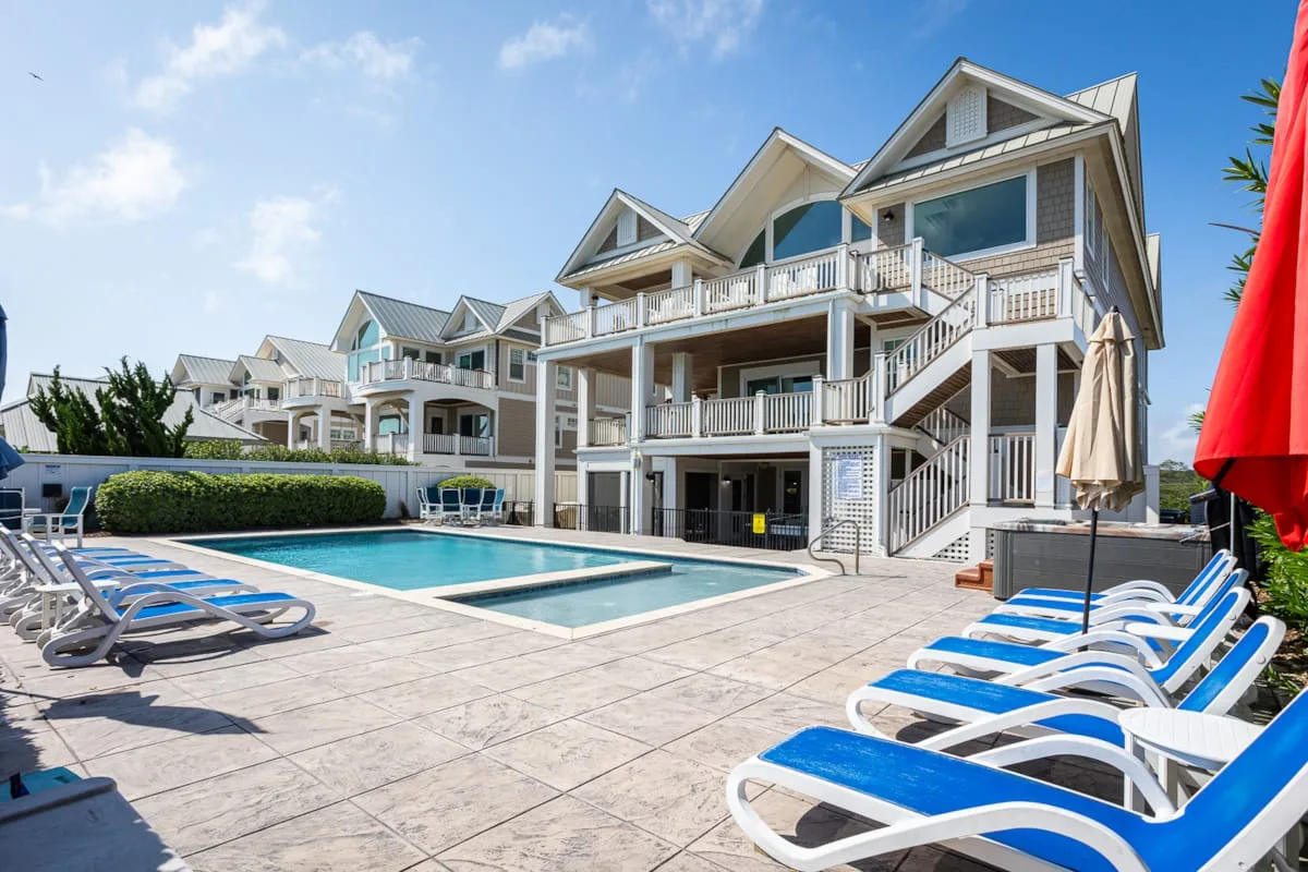 An outdoor swimming pool sits beside a multi-story building, with lounge chairs around the deck.