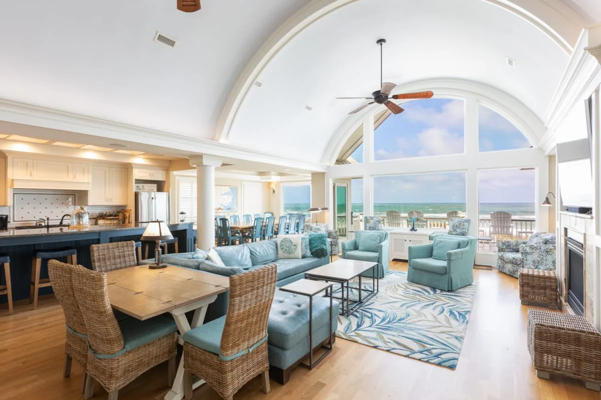A bright open living and dining area with seating and large windows overlooking the water.