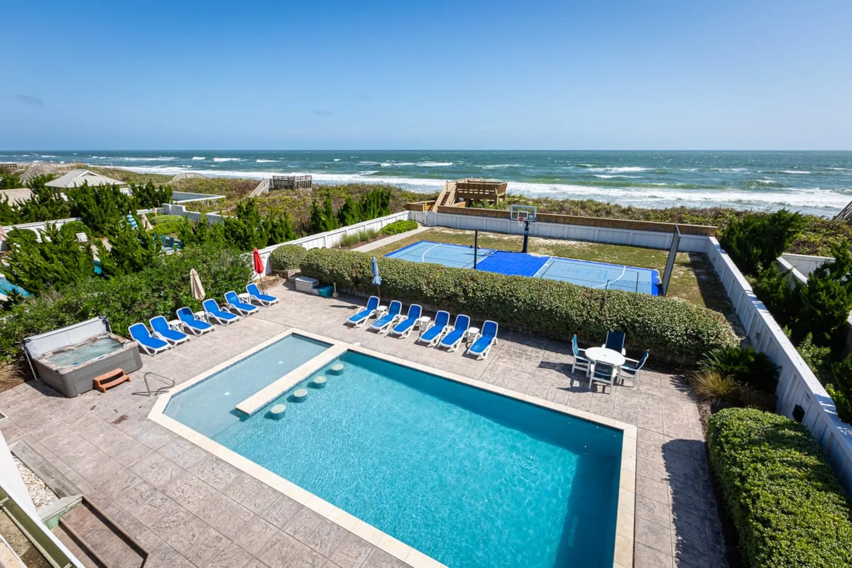 A swimming pool and tennis court sit beside the ocean.