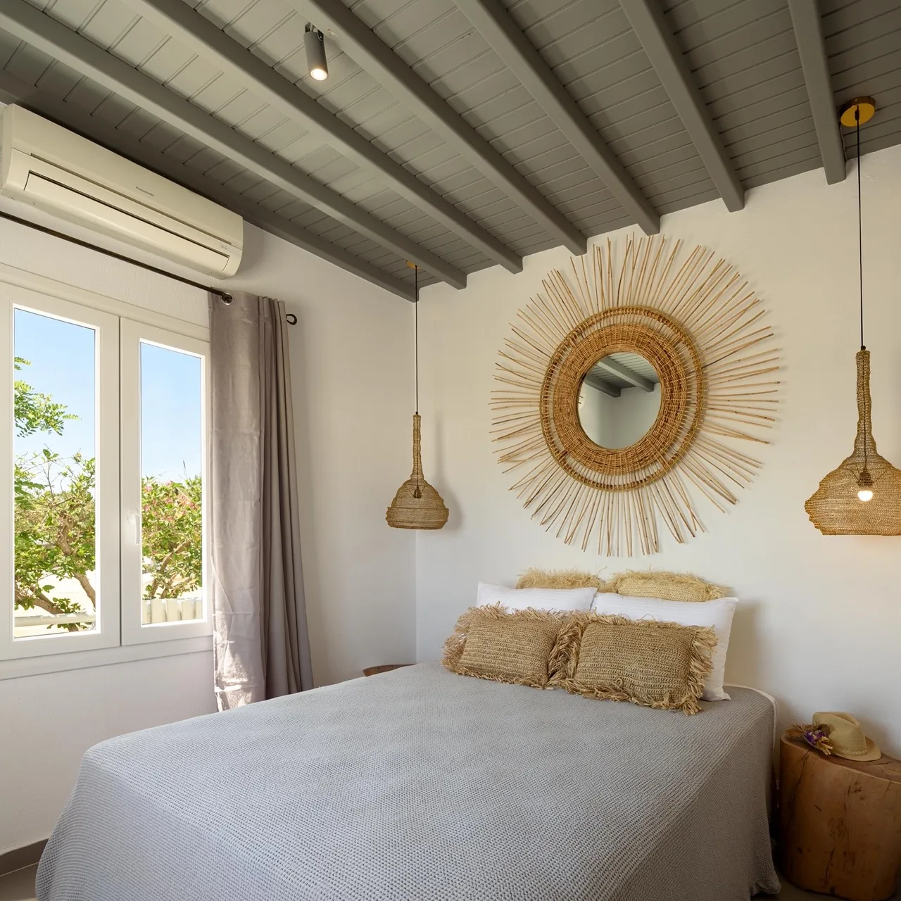 Un dormitorio luminoso con una cama bajo un espejo redondo con rayos.