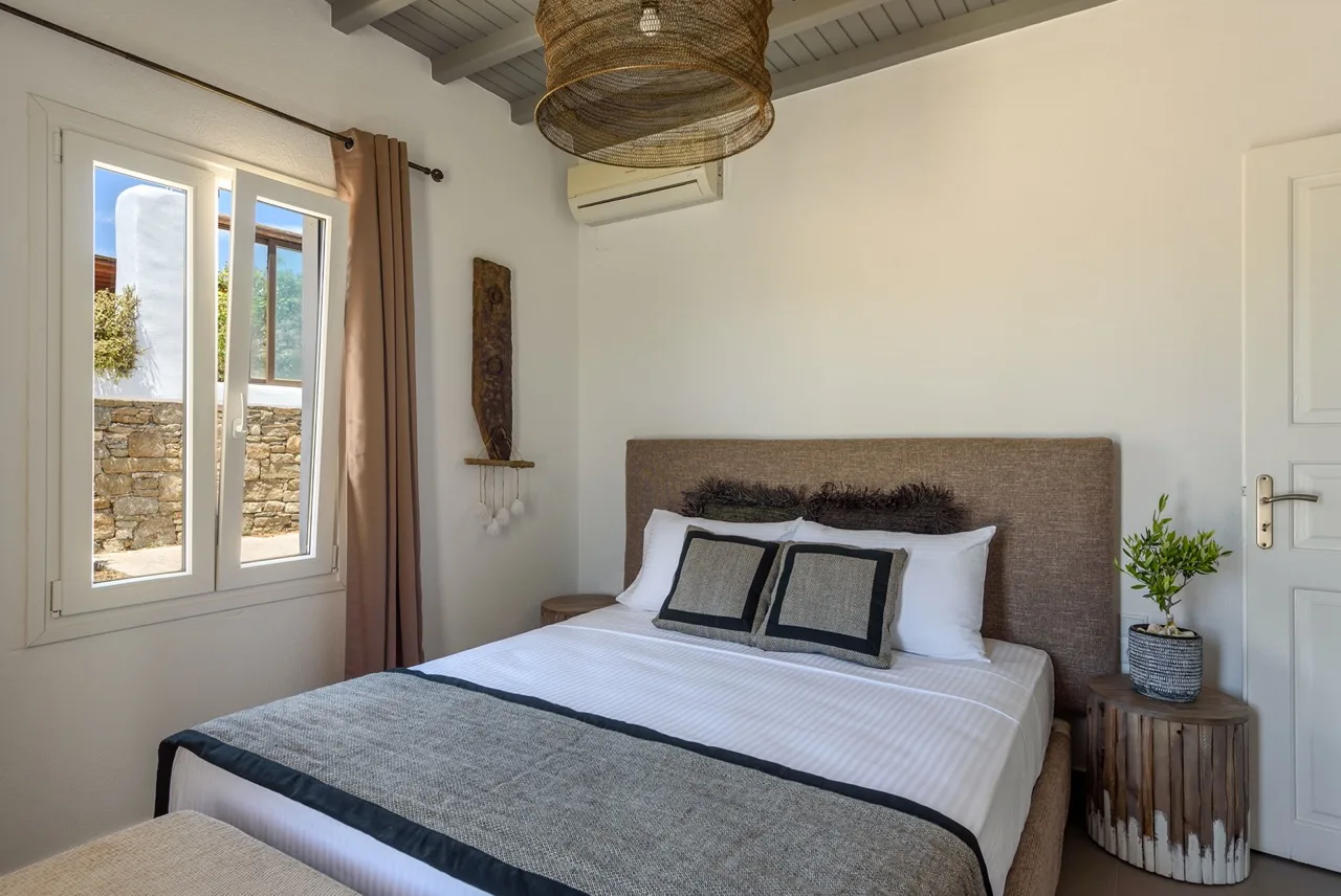 A bedroom with a neatly made bed and a window overlooking a stone wall.