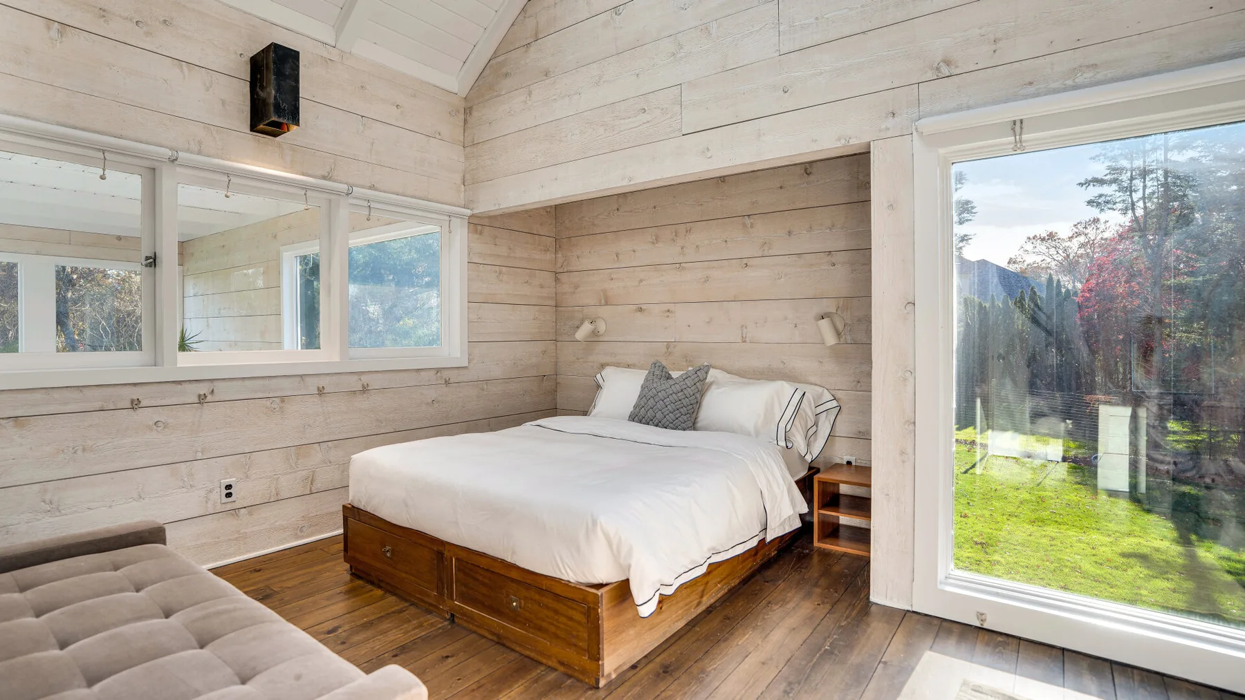 Un dormitorio con una cama, paredes de madera y una gran puerta de vidrio.