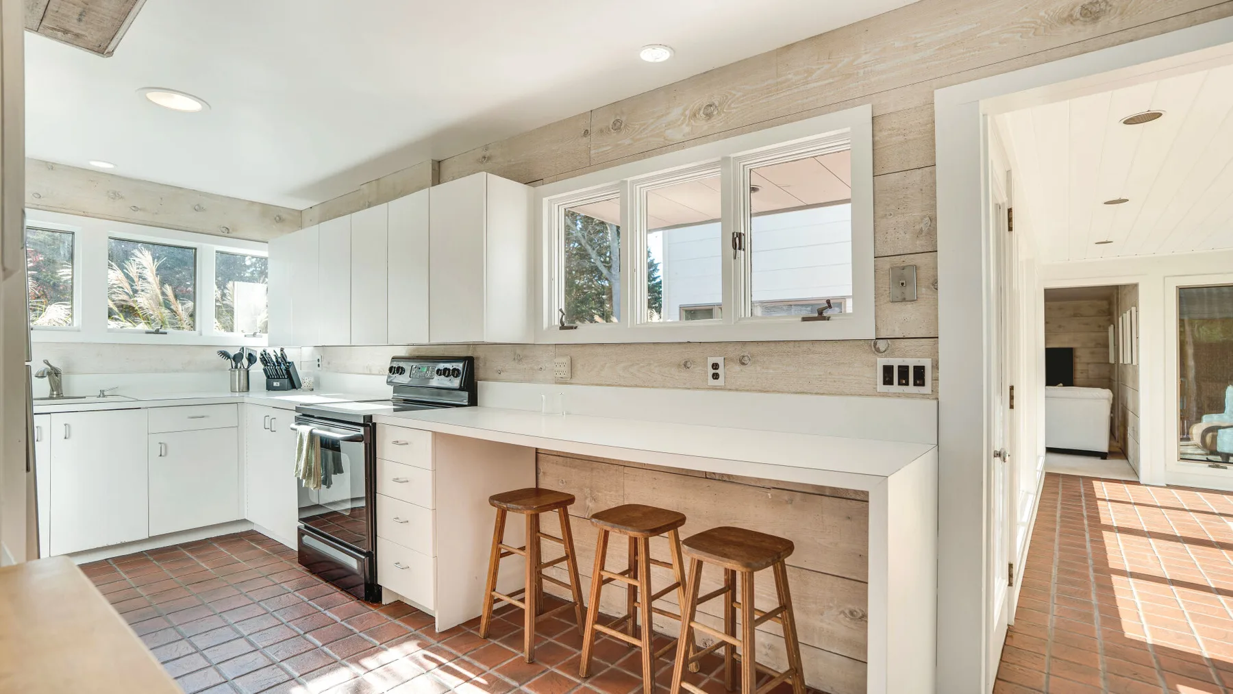 Una cocina luminosa con una encimera larga, gabinetes blancos y taburetes de madera.