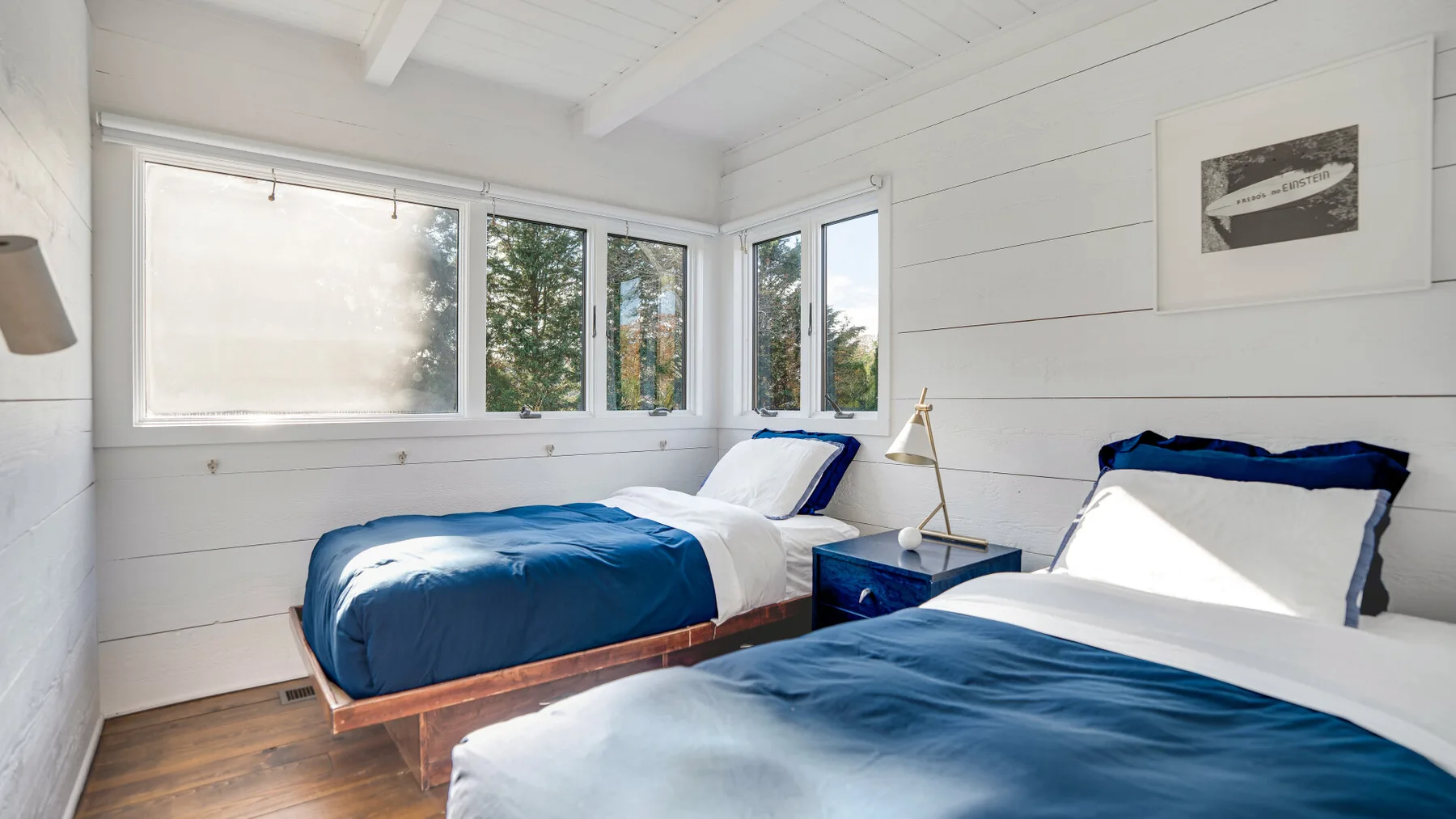 Un dormitorio luminoso con dos camas, ropa de cama blanca y ventanas grandes.