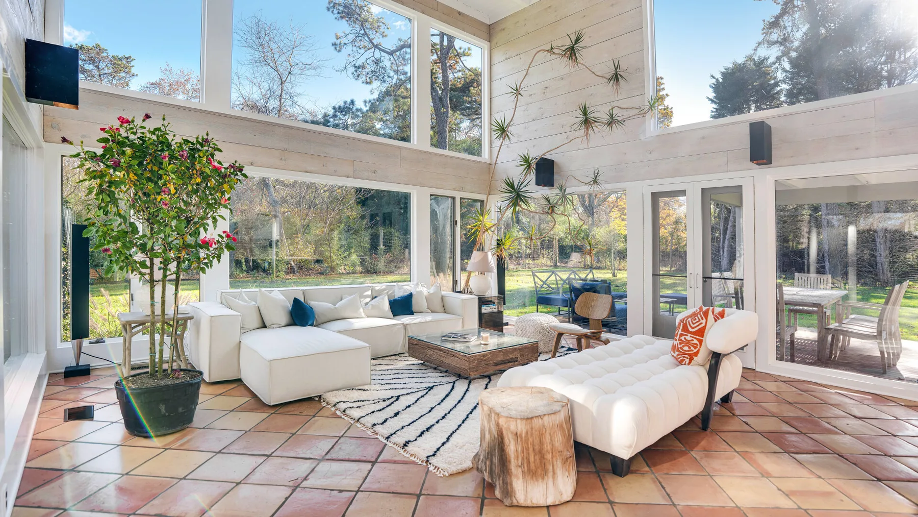 Una sala luminosa con grandes ventanas, asientos blancos y una mesa de centro baja.