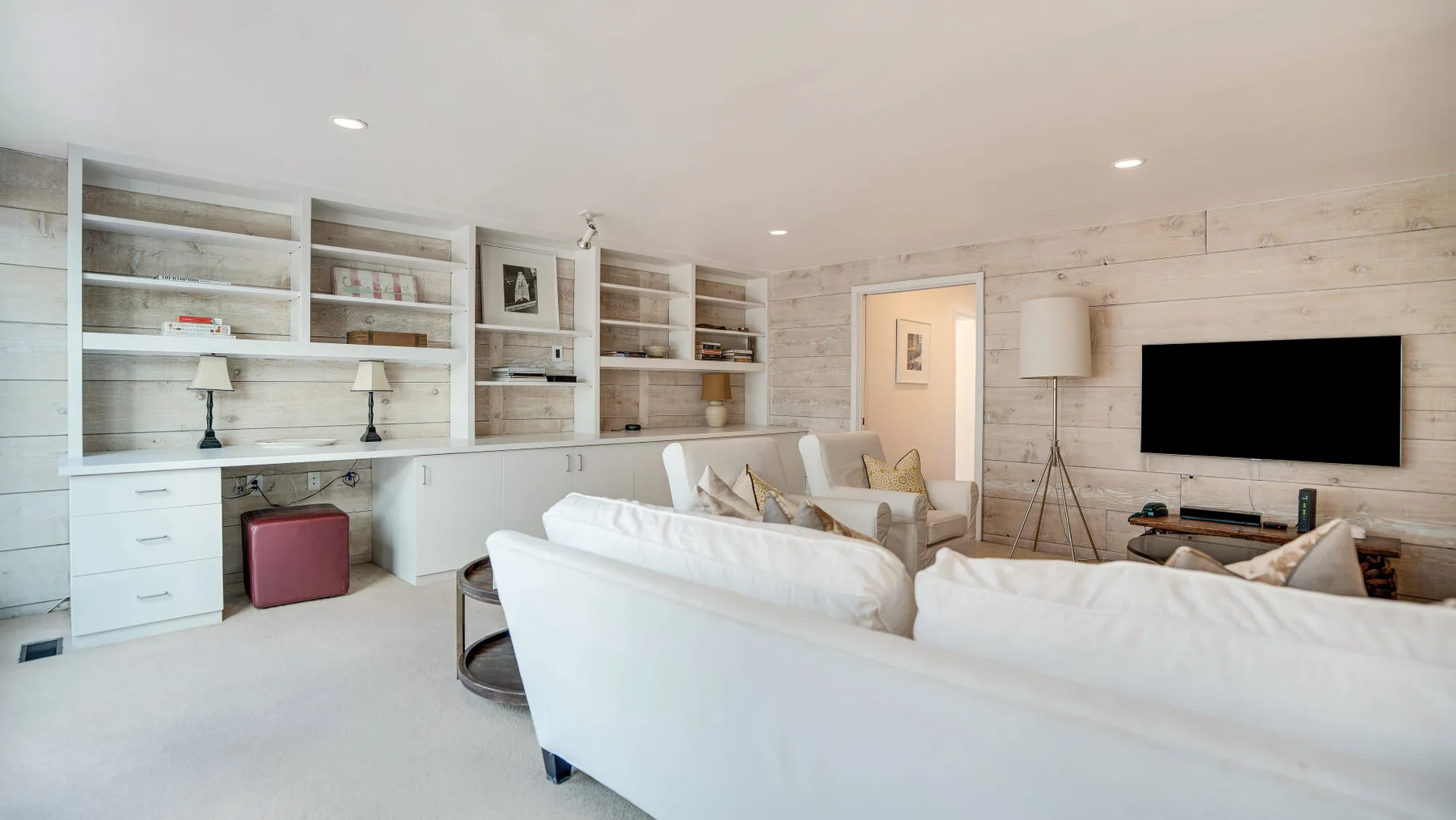 Una sala luminosa con asientos blancos, estantes empotrados y un televisor en la pared.