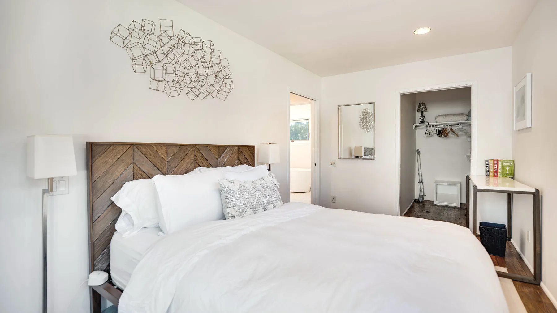 Un dormitorio luminoso con una cama bien tendida y decoración geométrica en la pared.