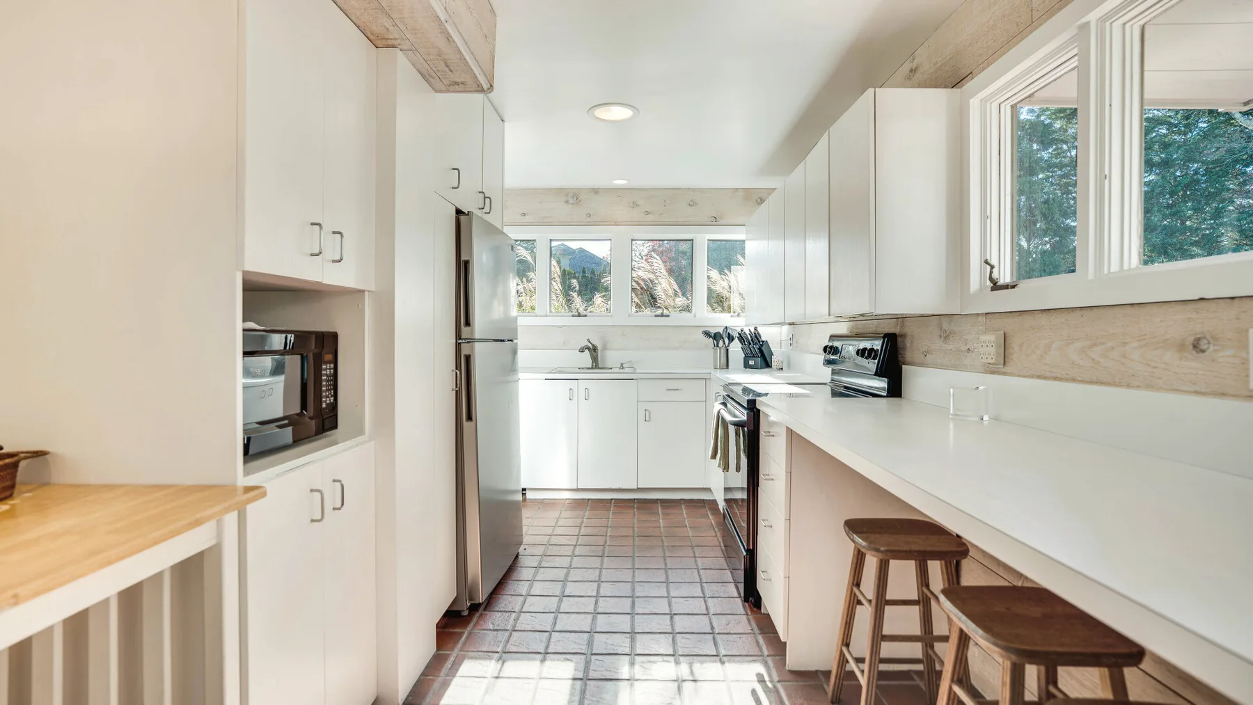Una cocina luminosa con gabinetes blancos, una encimera larga y ventanas.