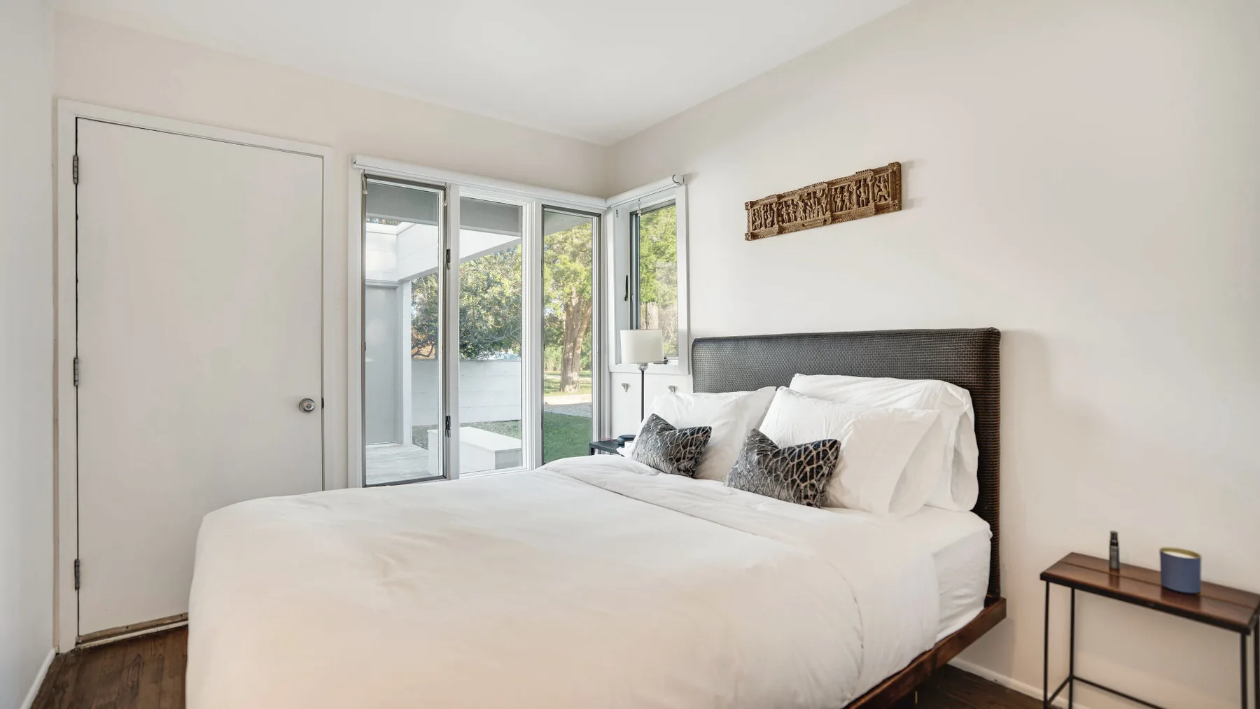 Un dormitorio luminoso con una cama tendida junto a puertas de vidrio que dan a un patio.
