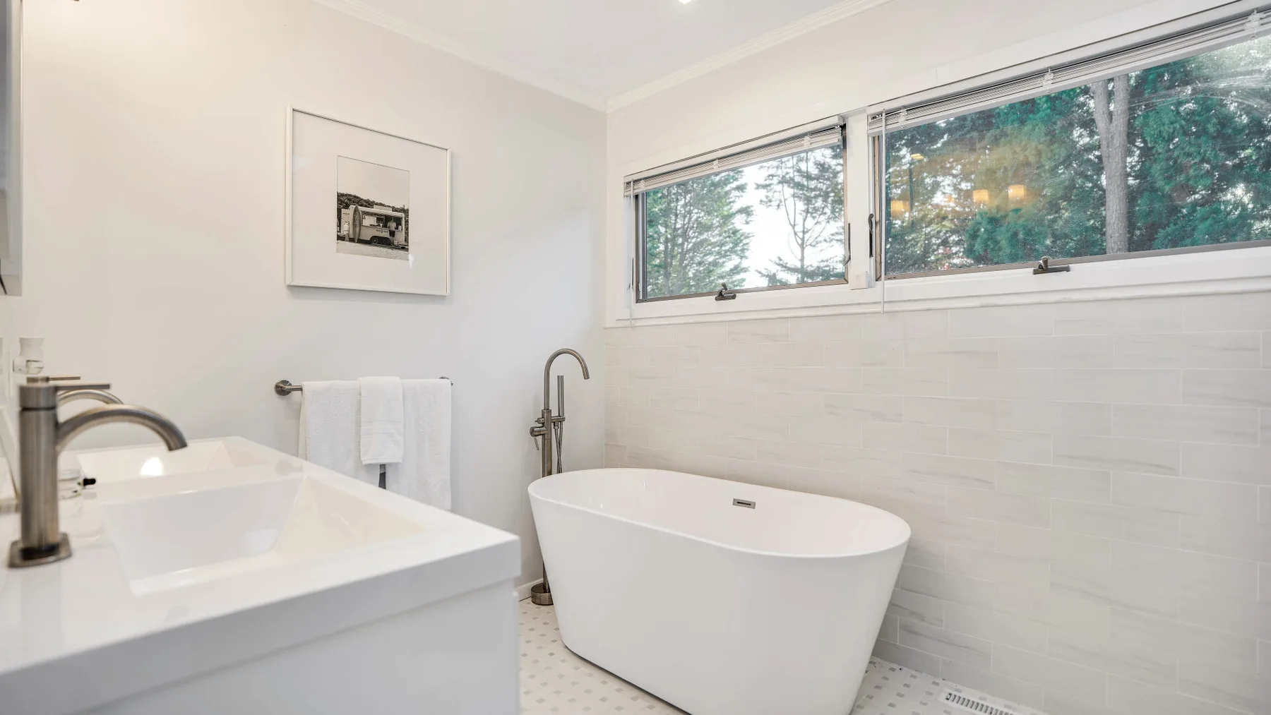 Un baño luminoso con una bañera exenta bajo una ventana amplia.