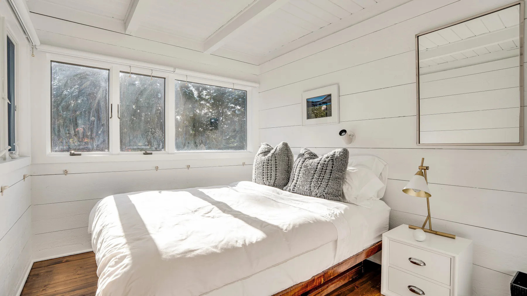 Un dormitorio luminoso con una cama bajo varias ventanas.