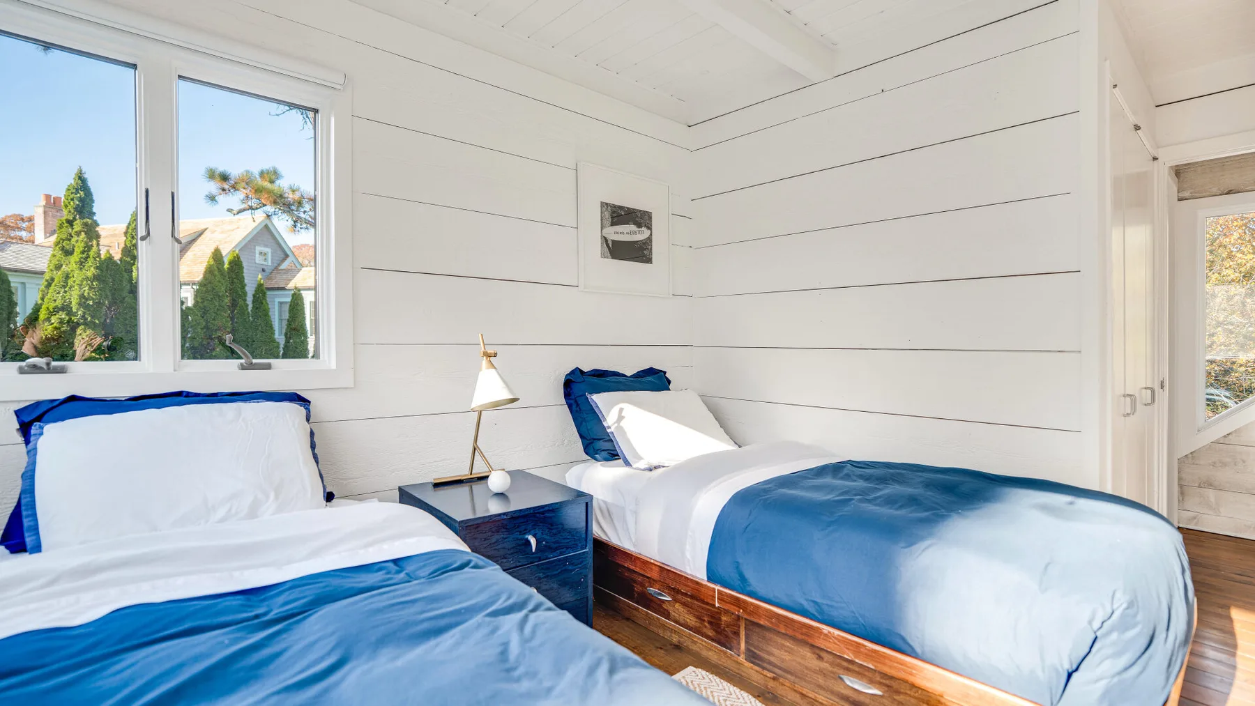 Un dormitorio luminoso con dos camas vestidas con ropa de cama azul y blanca.