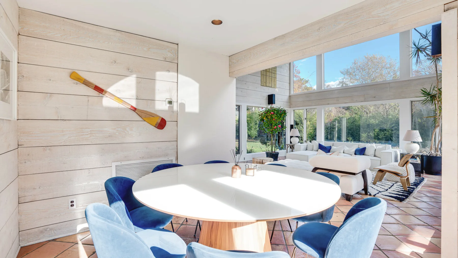 Un comedor luminoso con una mesa ovalada y asientos azules junto a grandes ventanas.