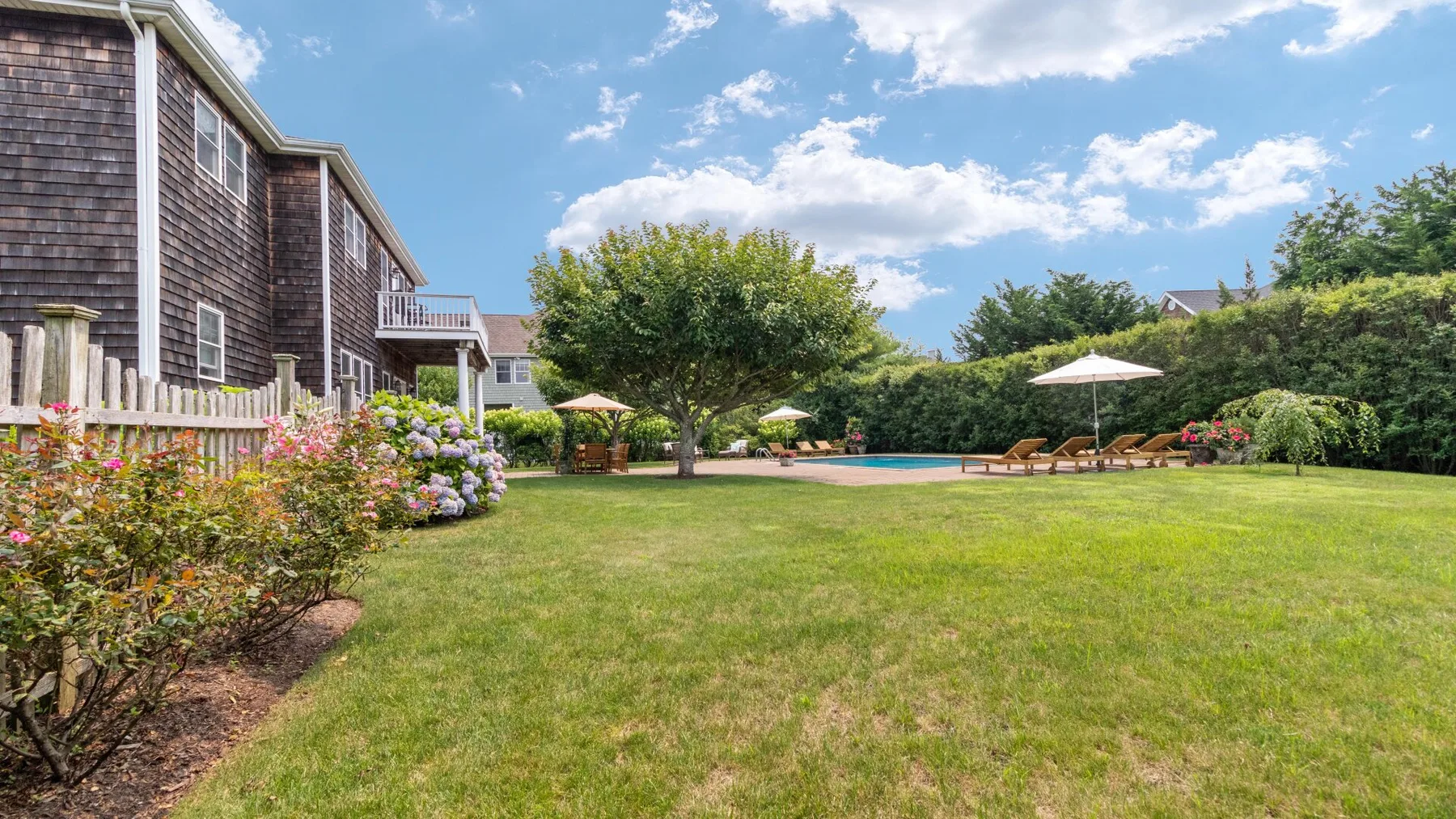 A landscaped backyard with a broad lawn, flowering shrubs, and a swimming pool.