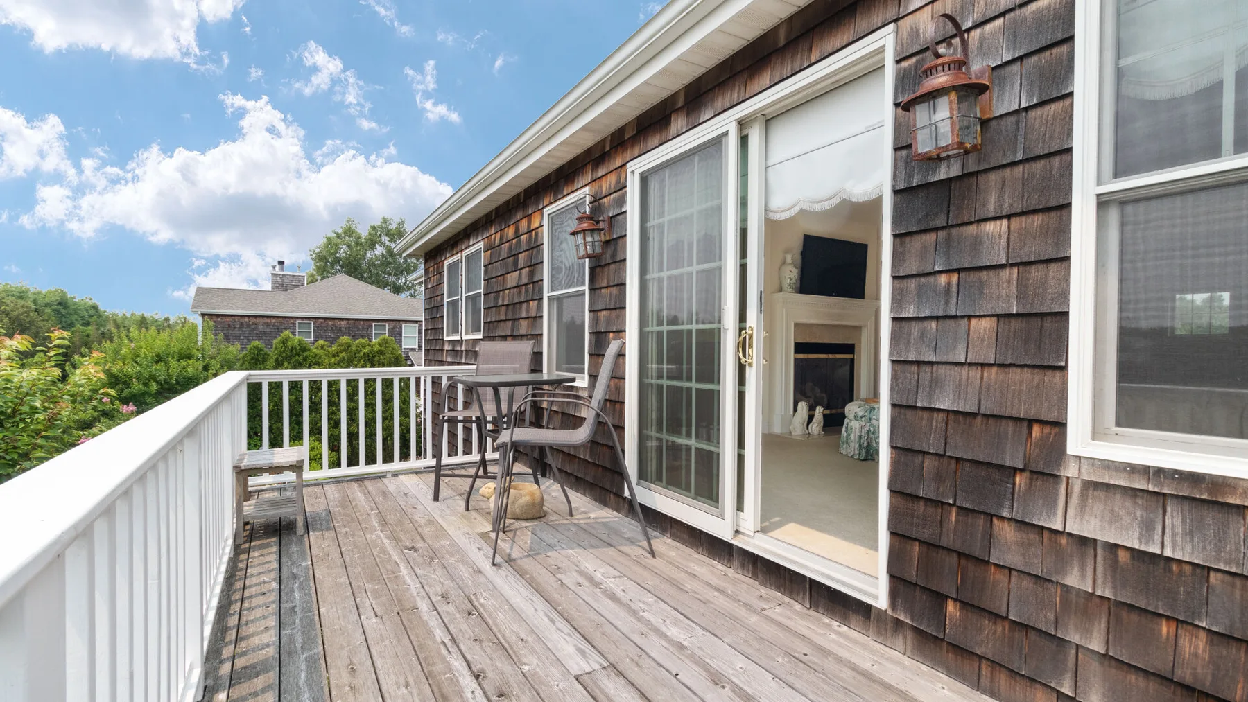 An outdoor deck with seating and a sliding glass door opening into a room.